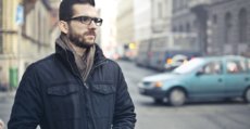 A young man with beard wearing glasses standing in the street