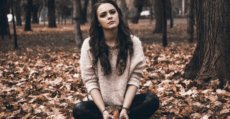A woman feeling sad sitting in a park surrounding by autumn leaves